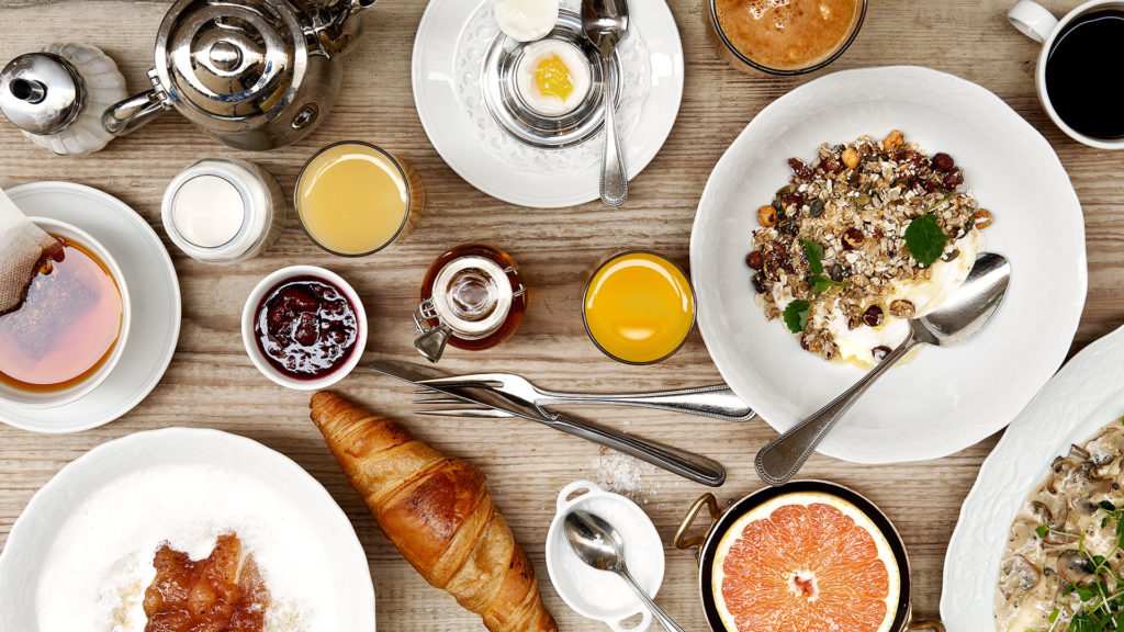 Dukat frukostbord ovanifrån med kaffe, juice, croissant, yoghurt med müsli och sylt